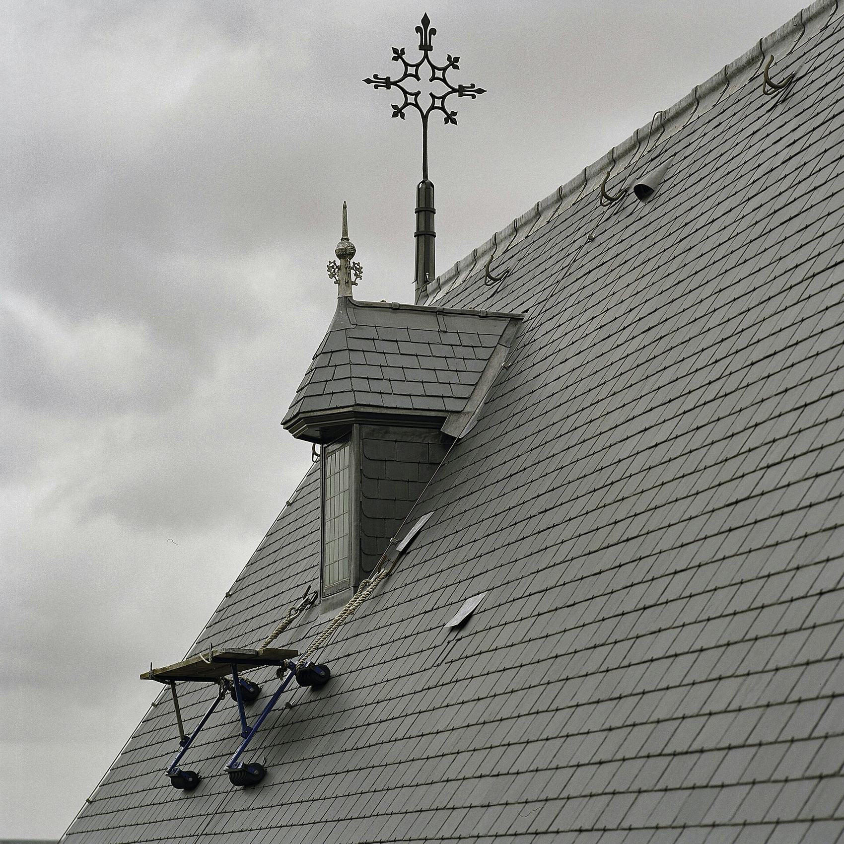 Toiture en ardoise avec lucarne et épi de faîtage sous un ciel gris